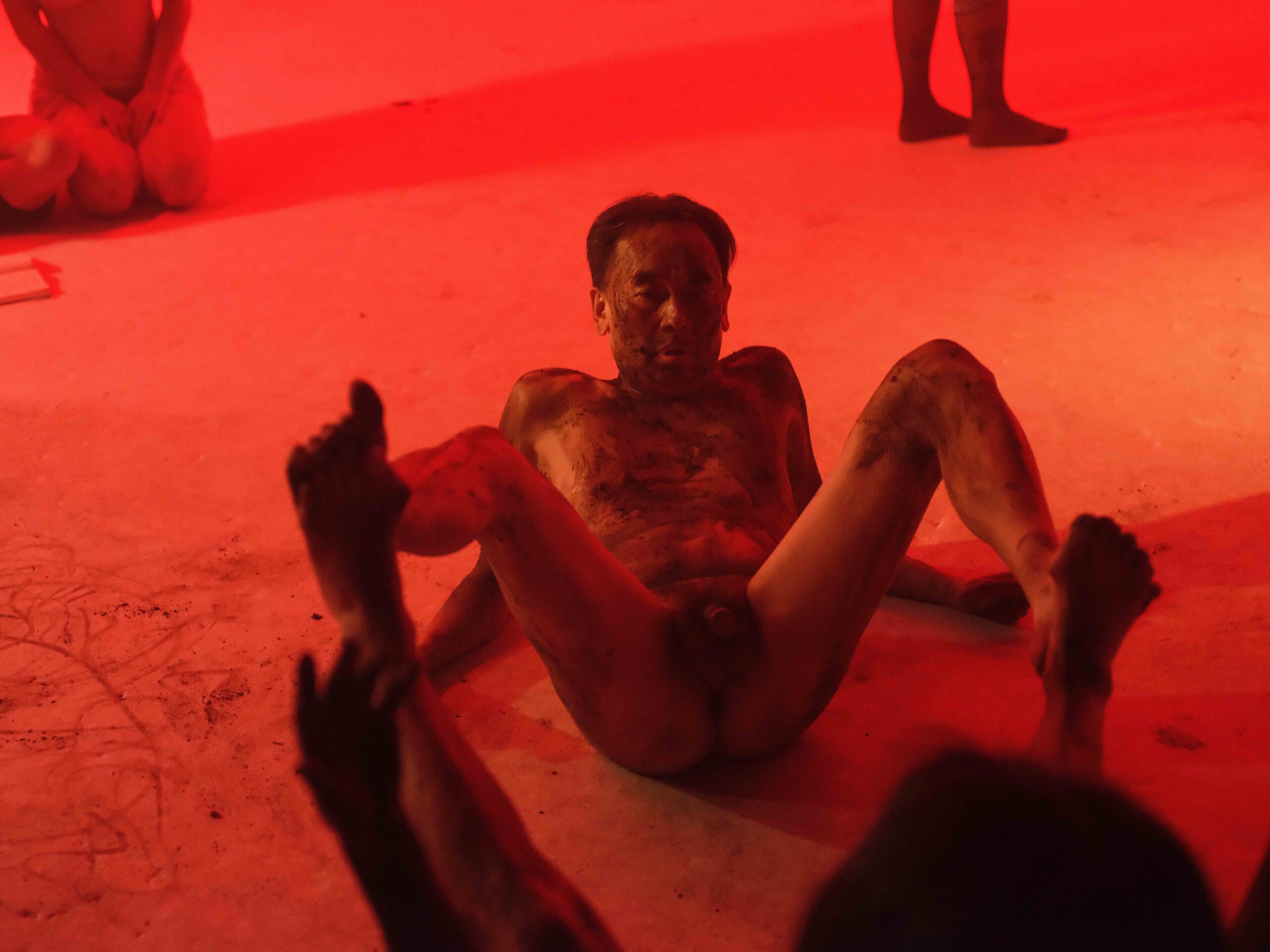 Dirt 5 Groep mensen in verschillende poses, waaronder een persoon in een rolstoel, op een lichtgekleurde vloer. De deelnemers zijn gedeeltelijk gekleed en tonen een variëteit aan lichaamstypes en -stijlen, met een focus op lichamen en interacties tussen hen.