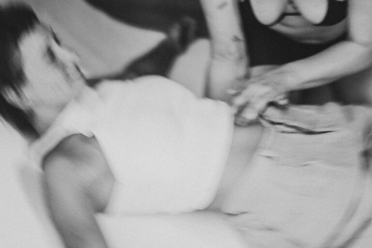 Een groep naakte mensen in een zwart-wit setting, gekleed in verschillende stijlen, die interactie hebben en in verschillende posities zijn geplaatst op een vloer met een heldere achtergrond, met enkele figuren die hun gezichten bedekken en anderen die elkaar omarmen.