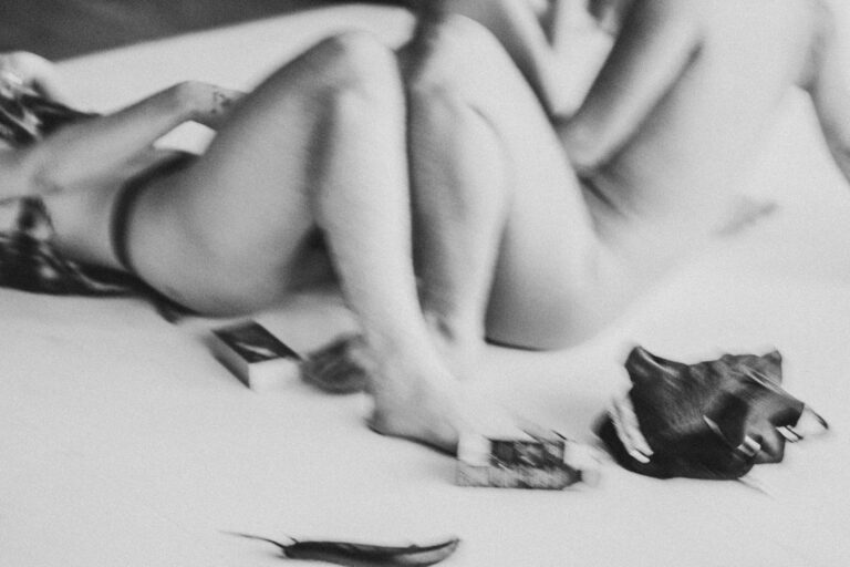 Een groep naakte mensen in een zwart-wit setting, gekleed in verschillende stijlen, die interactie hebben en in verschillende posities zijn geplaatst op een vloer met een heldere achtergrond, met enkele figuren die hun gezichten bedekken en anderen die elkaar omarmen.