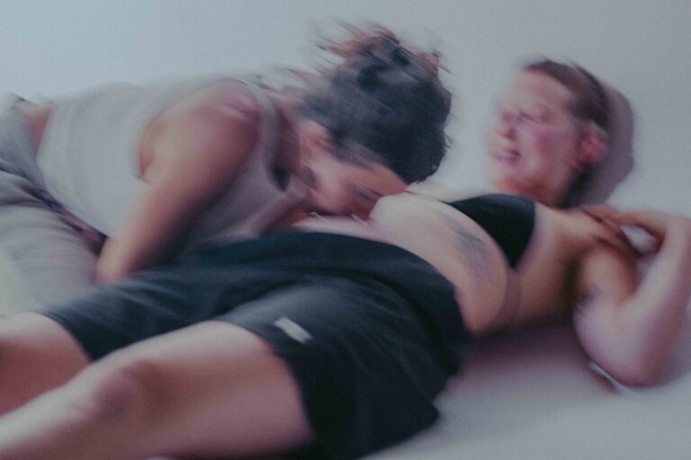 Een groep mensen die zich bezig houden met lichaamswerk of groepsinteractie, met een mix van naakte en geklede individuen die elkaar steun bieden en hun gevoelens delen in een sombere omgeving.