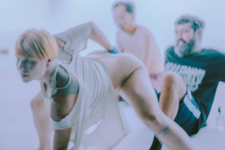 Een groep mensen die zich bezig houden met lichaamswerk of groepsinteractie, met een mix van naakte en geklede individuen die elkaar steun bieden en hun gevoelens delen in een sombere omgeving.