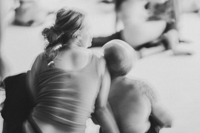 Een groep naakte mensen in een zwart-wit setting, gekleed in verschillende stijlen, die interactie hebben en in verschillende posities zijn geplaatst op een vloer met een heldere achtergrond, met enkele figuren die hun gezichten bedekken en anderen die elkaar omarmen.