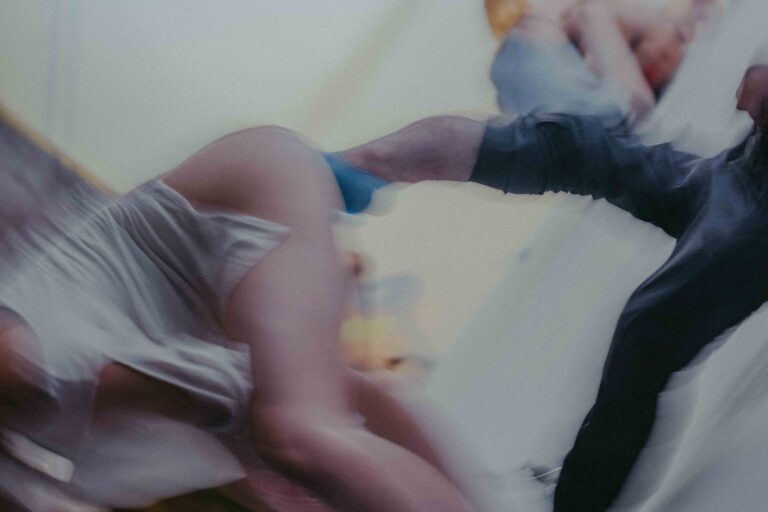 Een groep mensen die zich bezig houden met lichaamswerk of groepsinteractie, met een mix van naakte en geklede individuen die elkaar steun bieden en hun gevoelens delen in een sombere omgeving.