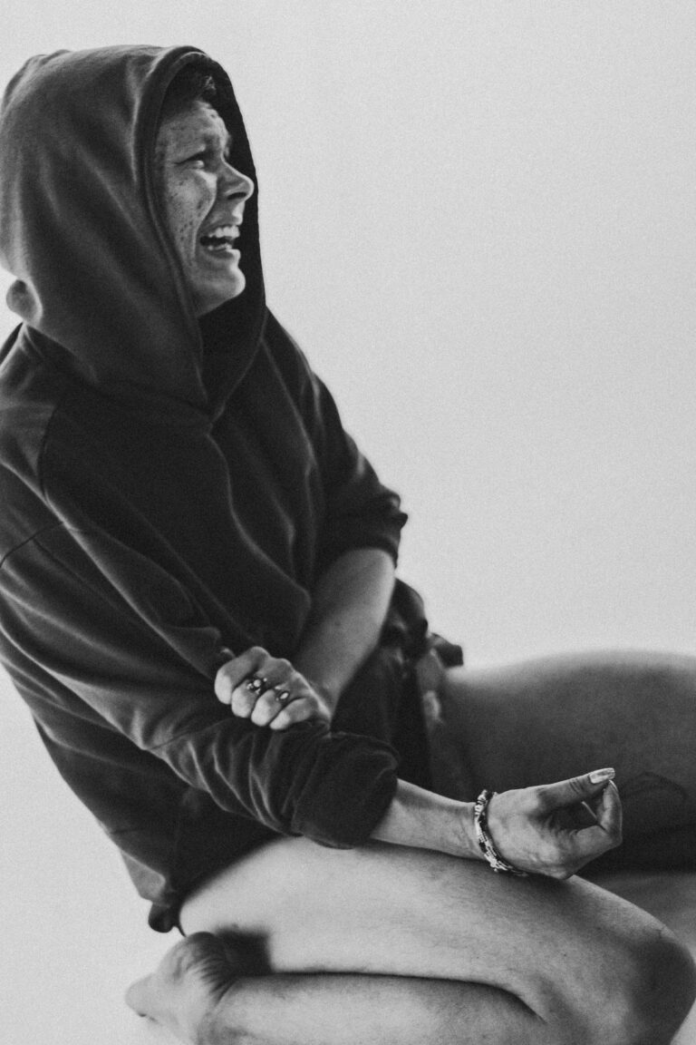 Naked person with a hooded cloak sitting in meditation pose looking to the side