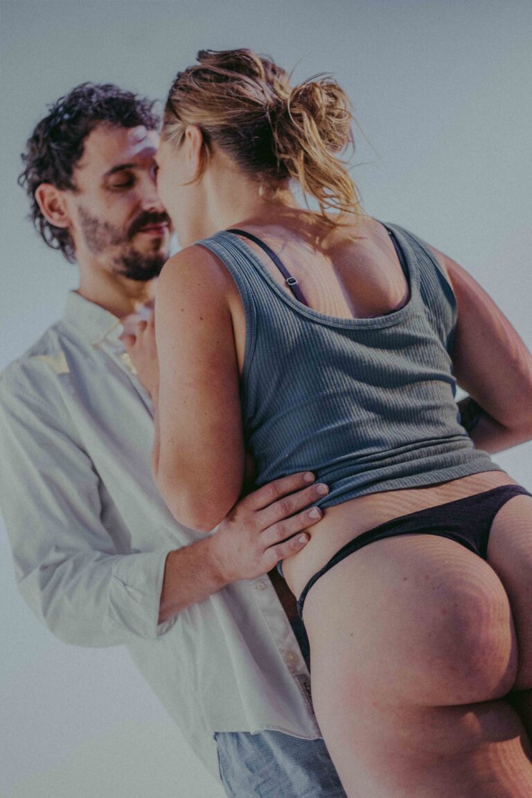 Two people in an intimate embrace, one with bare back and legs visible, captured in an abstract aesthetic with soft neutral tones.