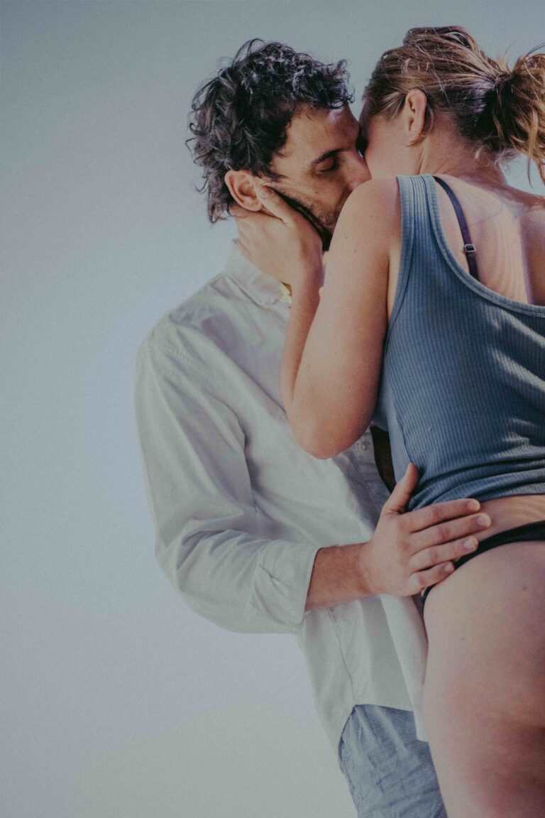 Two people in an intimate embrace, one with bare back visible, captured in an abstract aesthetic with soft gray and blue tones.