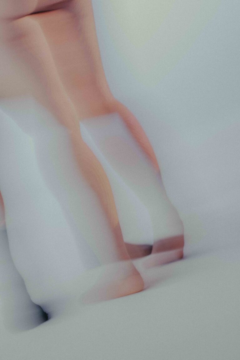 An abstract depiction of the bare legs of a nude person in motion, captured with heavy motion blur in soft pink and white tones.