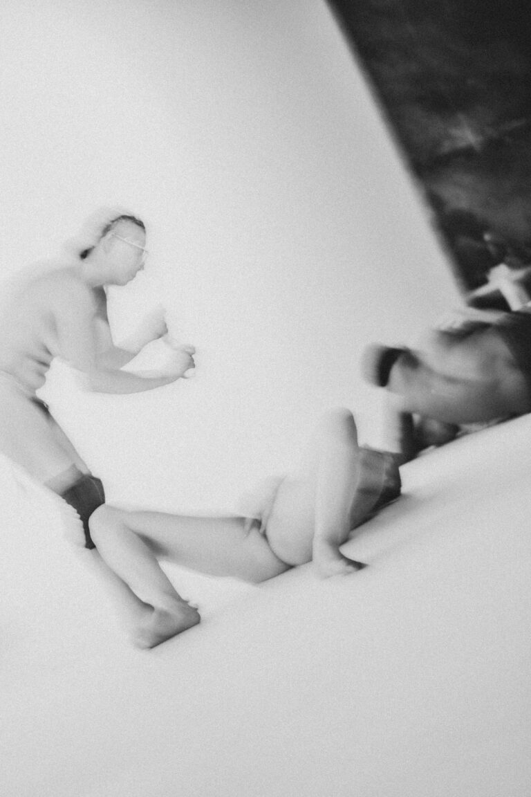 Two naked people in a combative dance pose on a performance stage with one person reaching upward