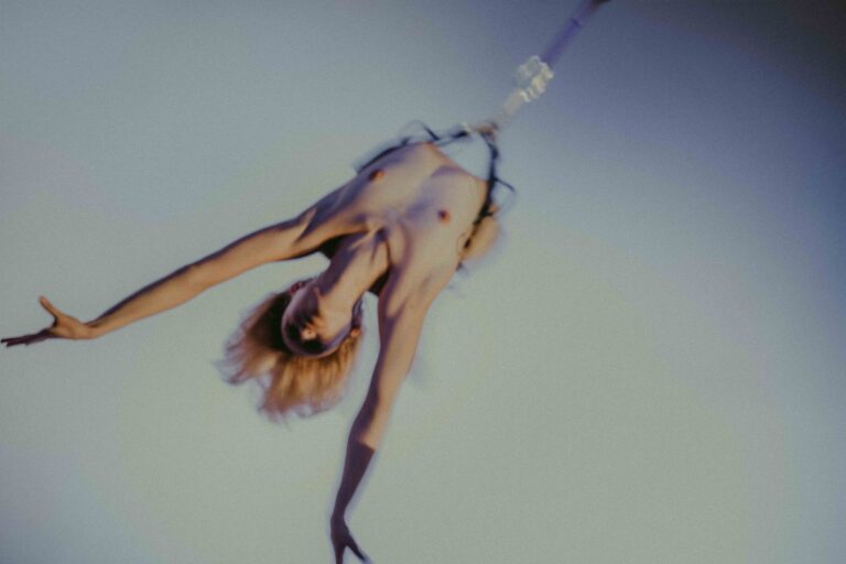 Een groep mensen die zich bezig houden met lichaamswerk of groepsinteractie, met een mix van naakte en geklede individuen die elkaar steun bieden en hun gevoelens delen in een sombere omgeving.