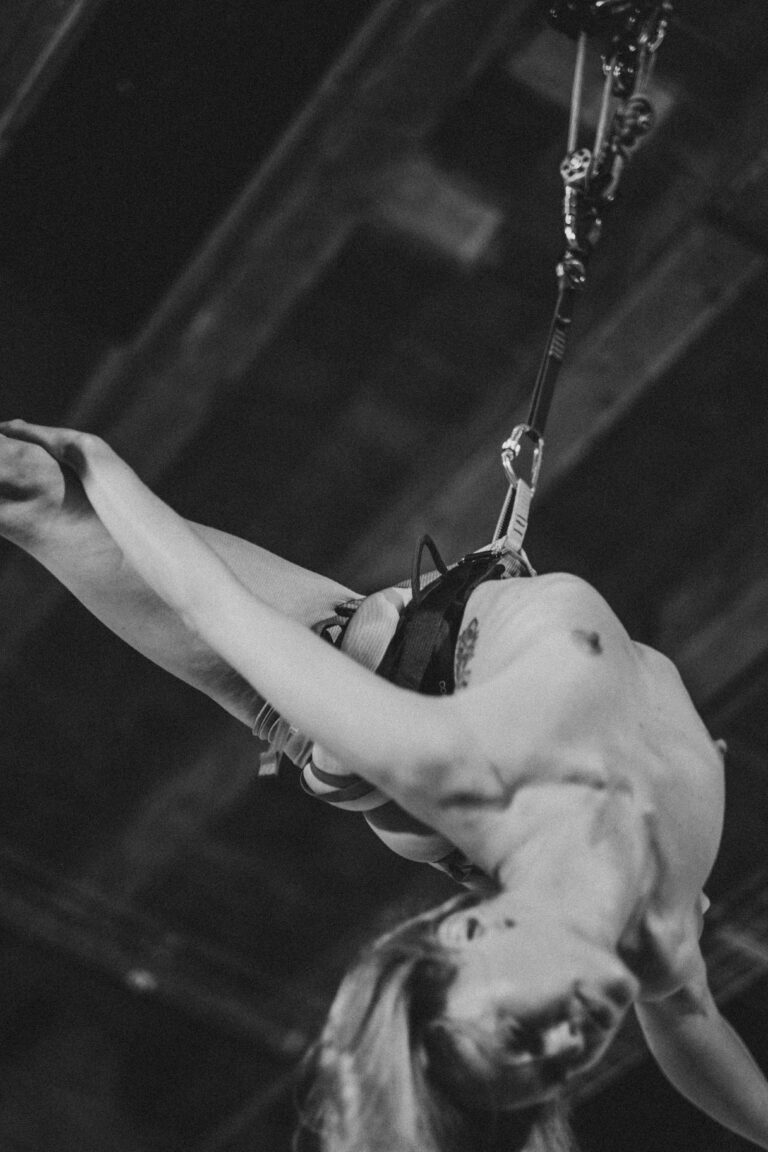Naked person hanging upside down from chains in dramatic black and white with arms gripping the chains