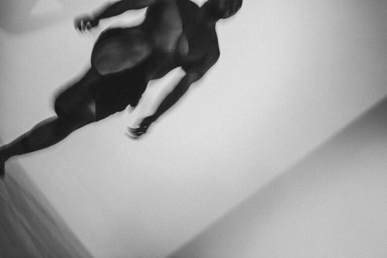 Een groep naakte mensen met Philemon Mukarno die elkaar ondersteunen in een acrobatische houding, met een persoon in het midden die door anderen wordt vastgehouden. De foto is in zwart-wit en geeft een artistieke sfeer weer, met een focus op de menselijke vormen en bewegingen.