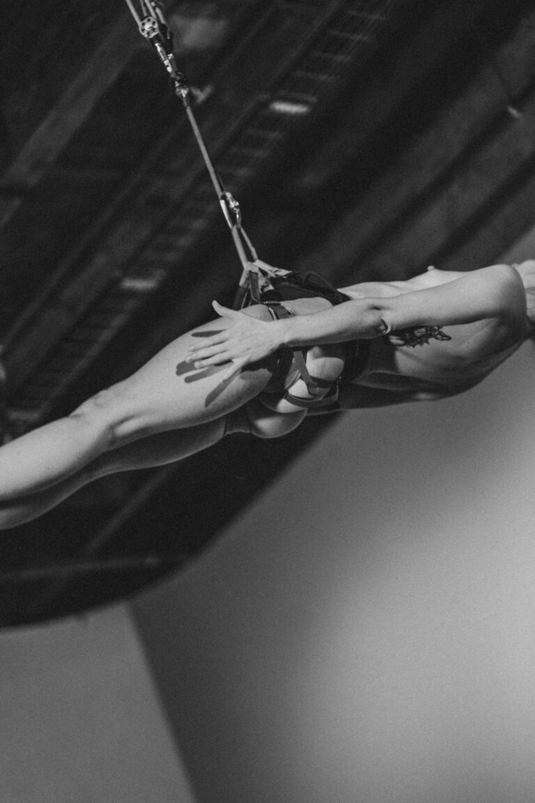 Naked person hanging from a rope making expressive hand gestures in close-up