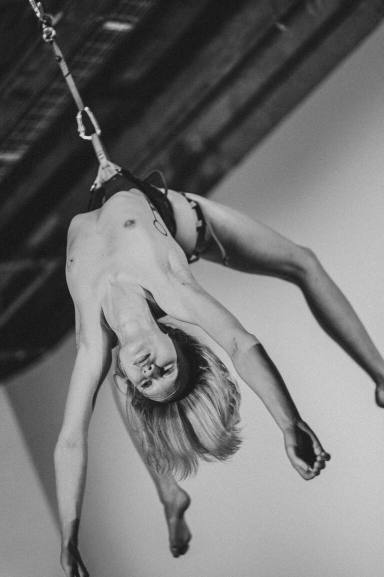 Naked person hanging upside down from chains in an aerial performance with hair flowing downward
