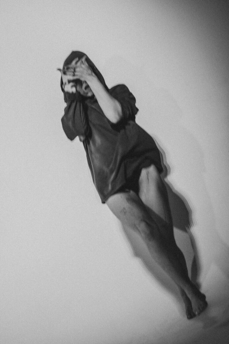 Naked person in an oversized black shirt leaping in an expressive performance pose with arms raised