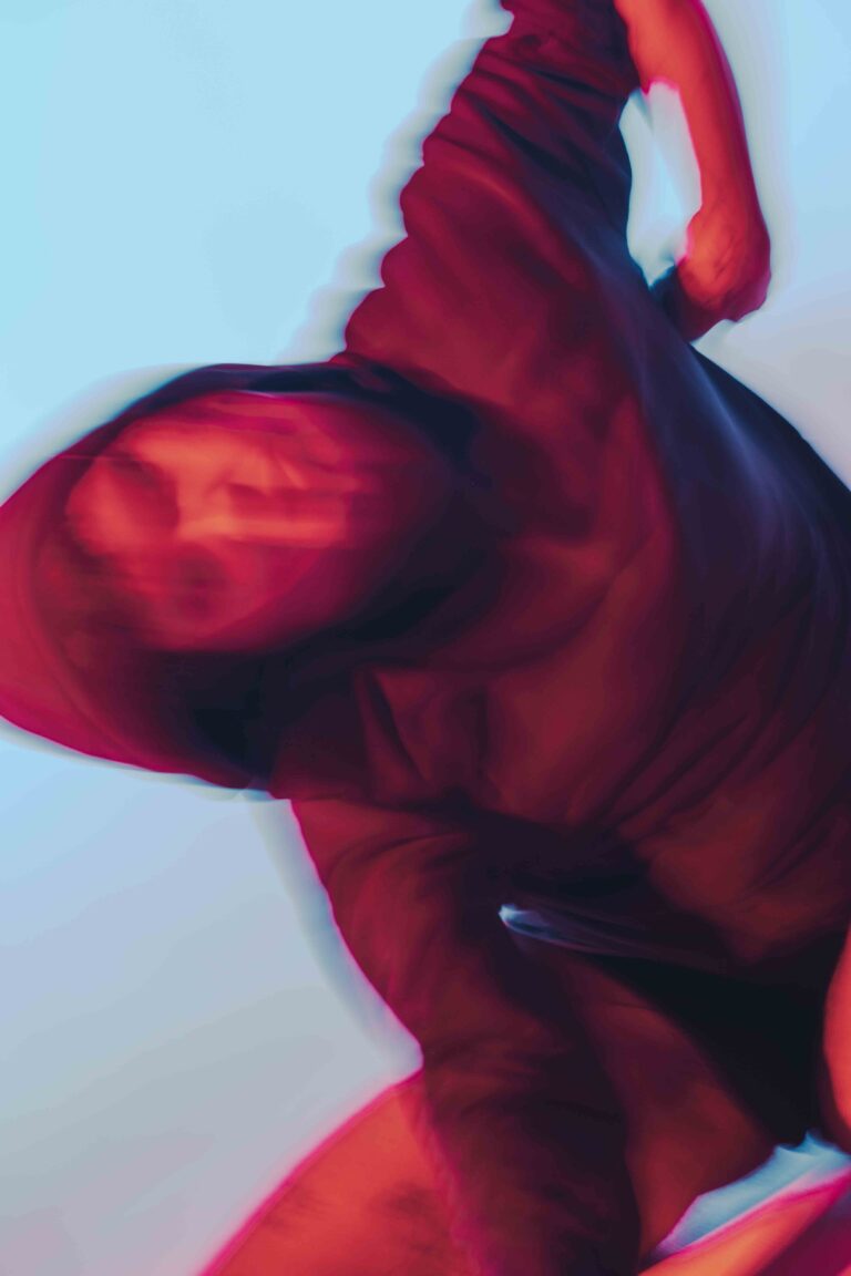 Moving nude figures from behind with an abstract and colorful aesthetic, captured in vibrant red and purple tones with motion blur.