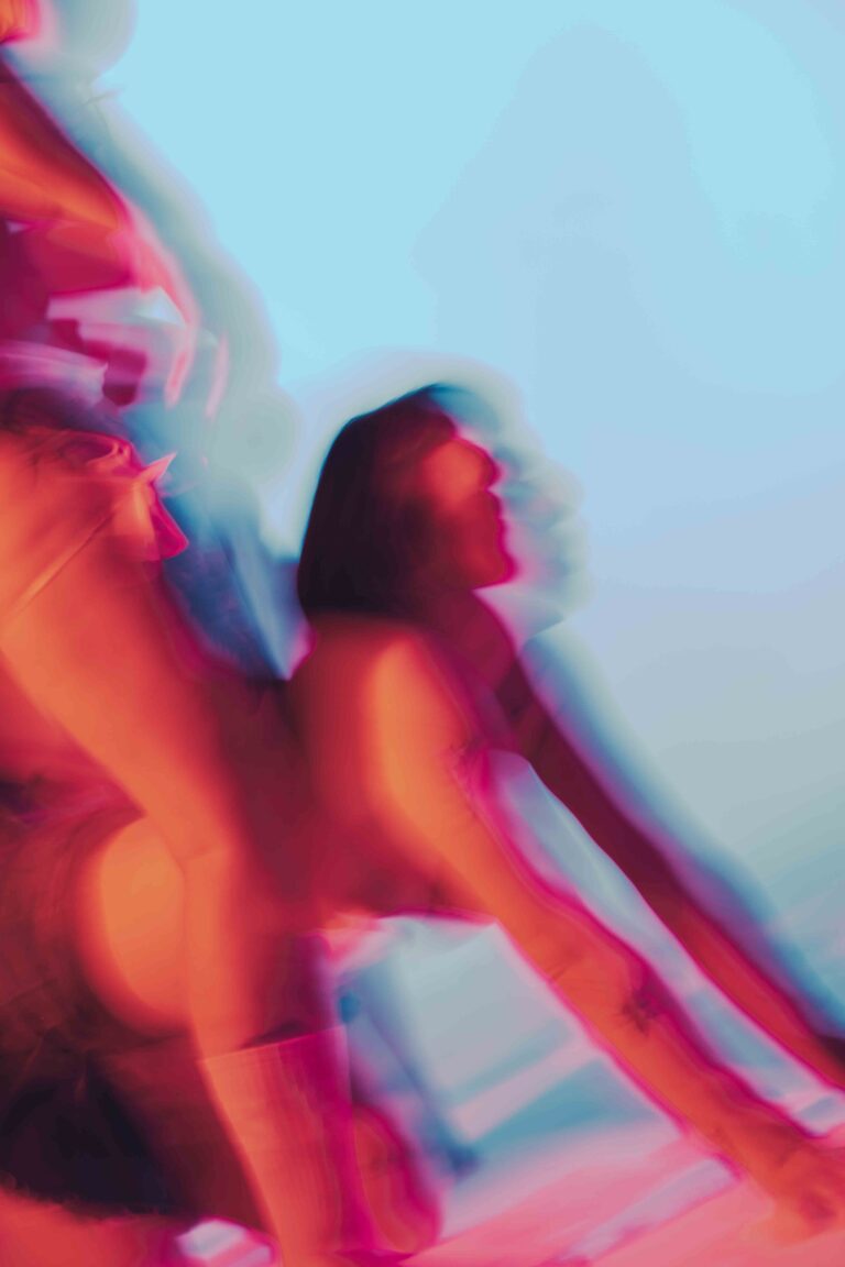 Moving nude figures with an abstract and colorful aesthetic, captured in vibrant red, pink and orange tones with dynamic motion blur.