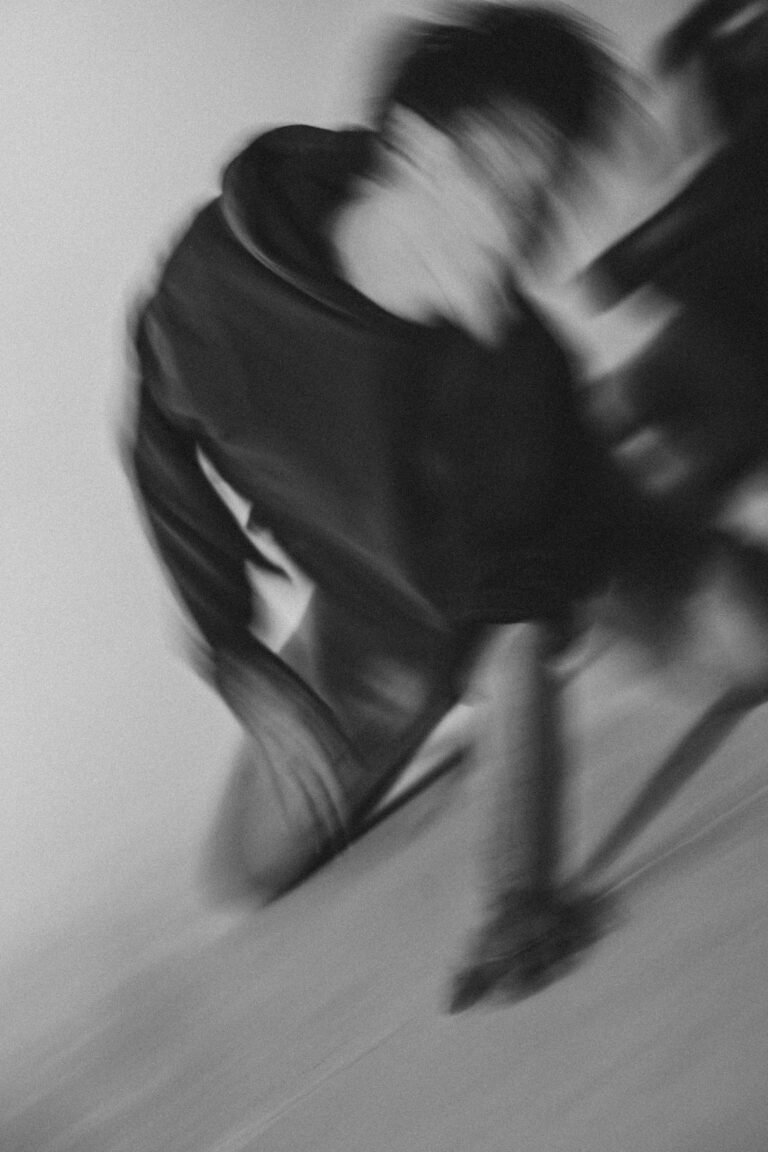 Blurred motion image of a naked person in black hoodie performing expressive movement