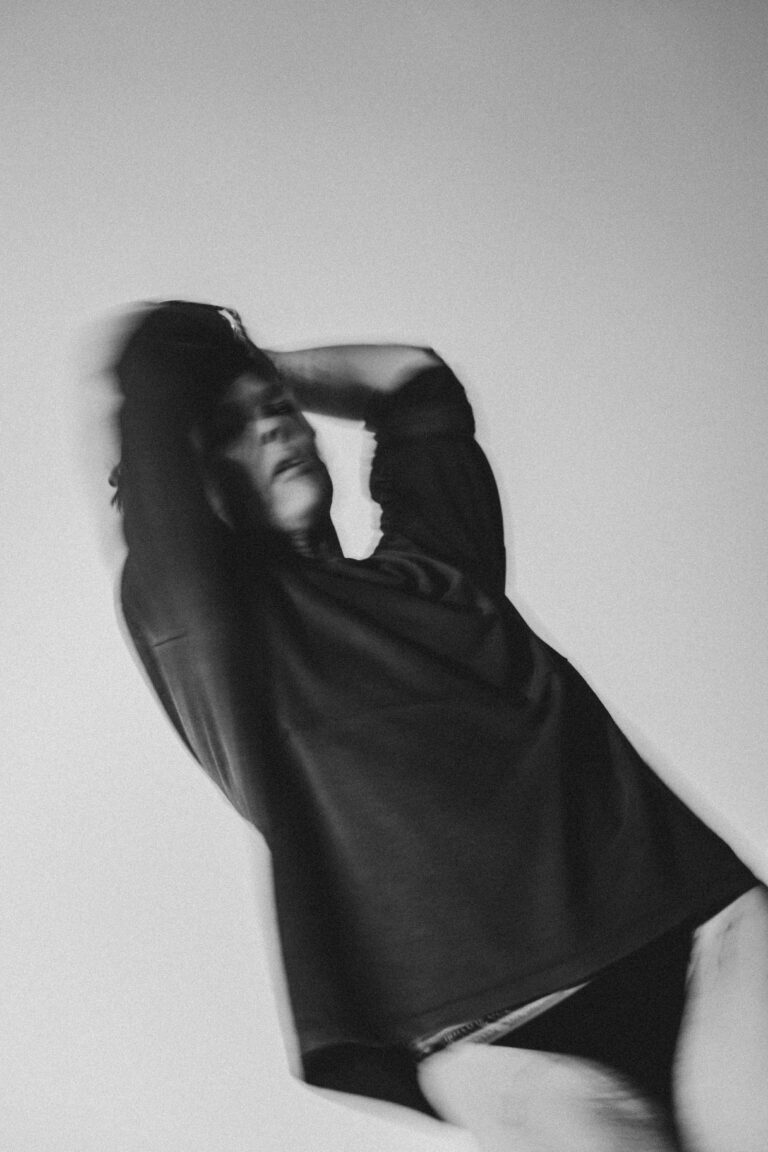 Black and white silhouette of a naked person in an expressive pose with arms raised to head