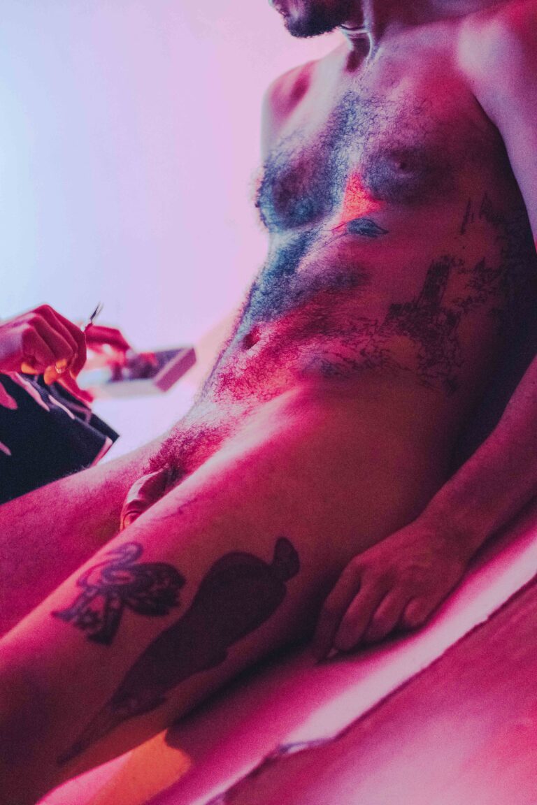 Profile view of nude male torso with visible tattoos, head tilted back in intense pink lighting
