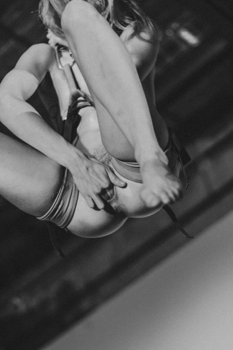 Naked woman in an acrobatic pose suspended from chains hanging upside down in the air