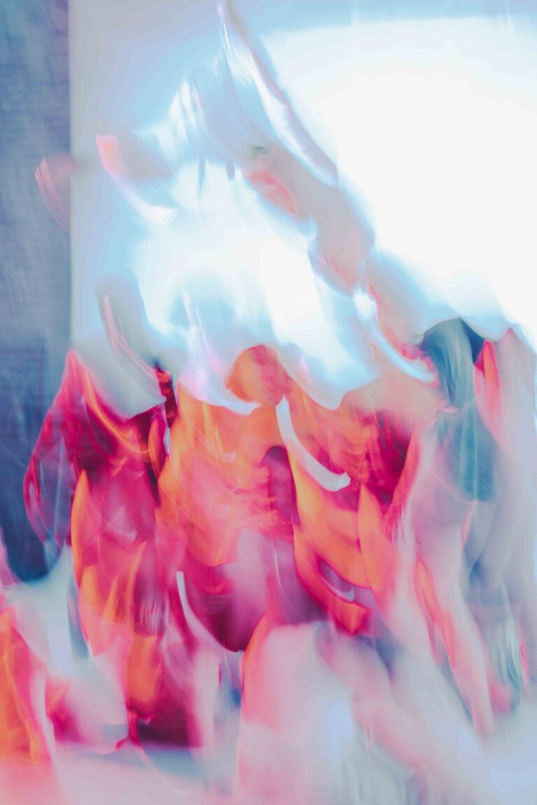 Motion-blurred group of nude performers on stage in vibrant pink and blue lighting