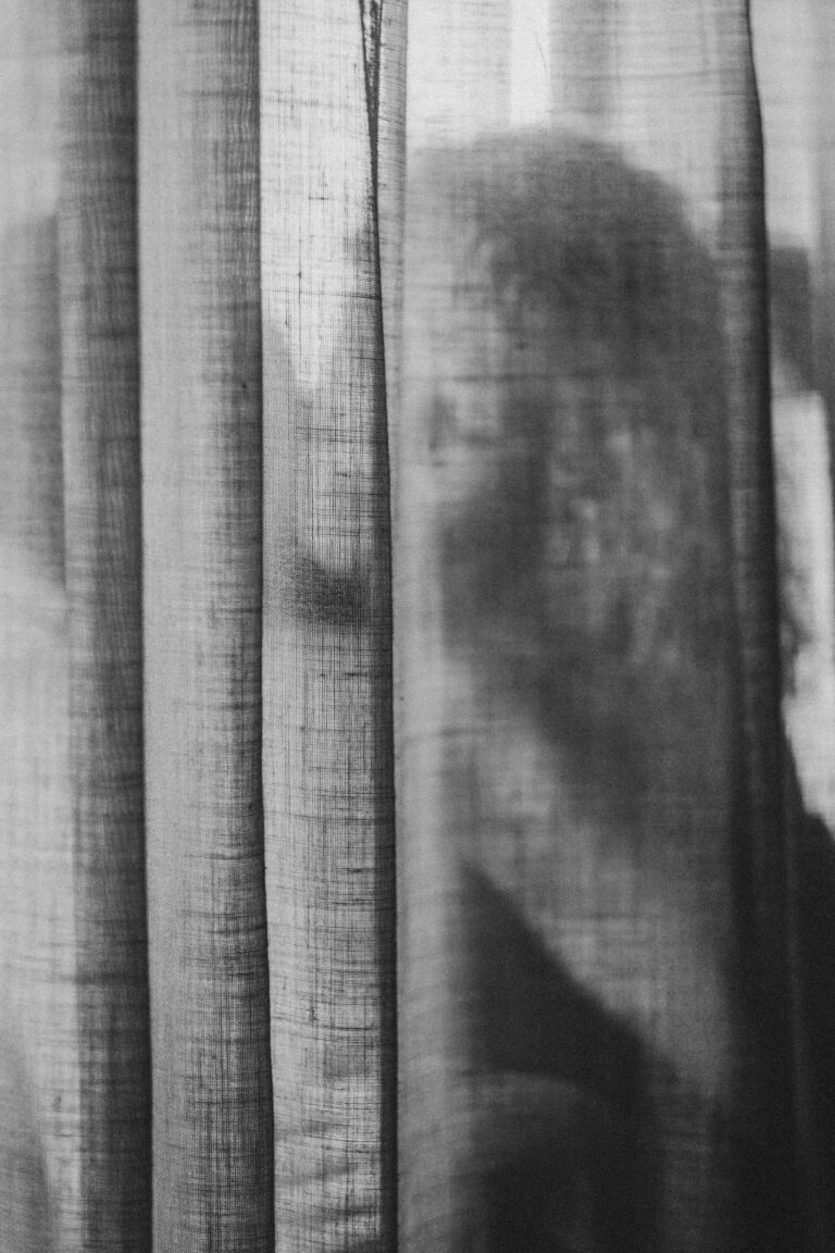 Black and white photo of transparent curtains with a naked silhouette partially visible through the fabric