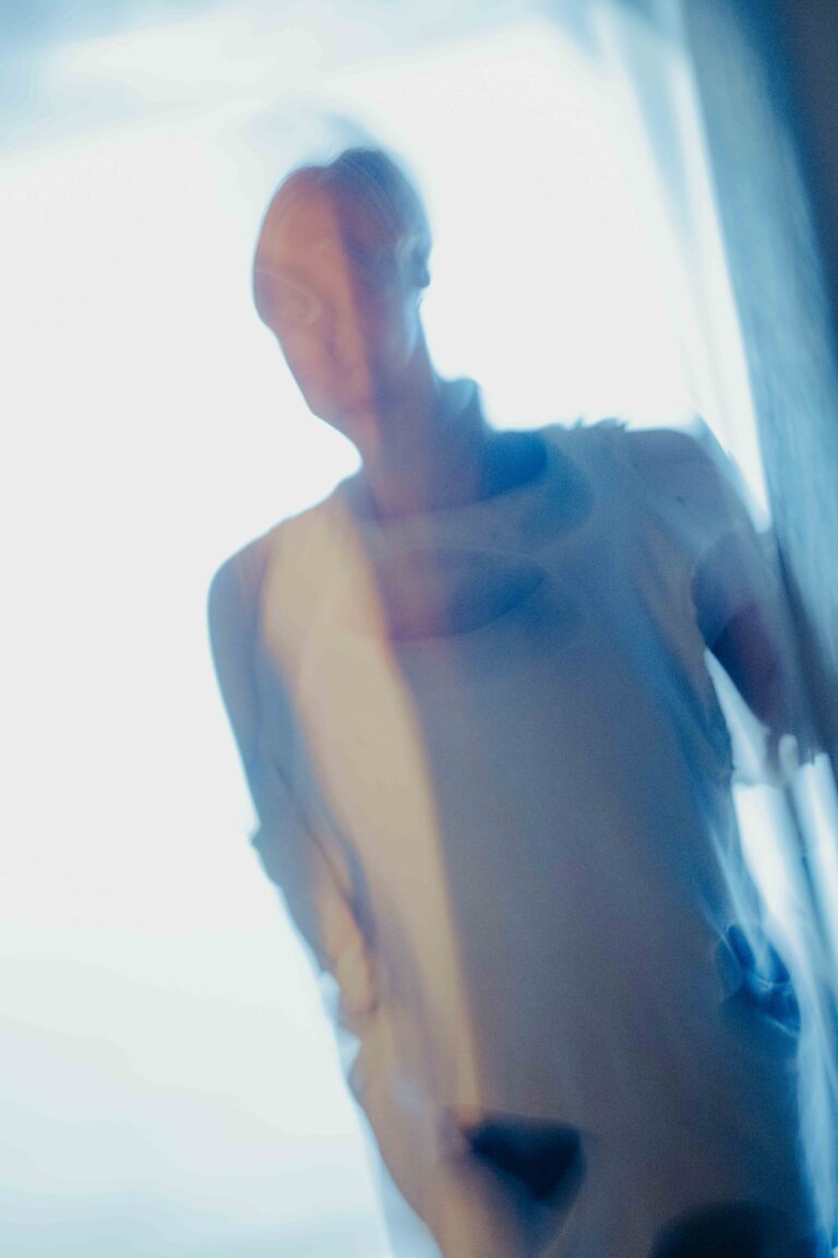 Blurred abstract image showing partial nude form in soft blue and white tones