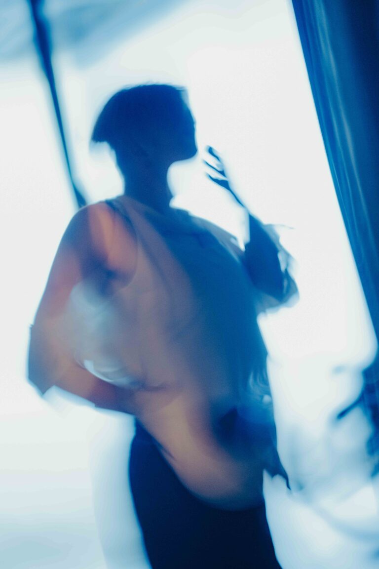 Blurred silhouette of a nude person with hand raised in dramatic blue and white lighting