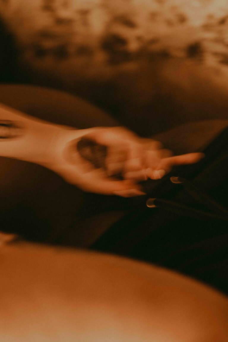 A tattooed hand holds a furry object against a nude torso in warm, dim lighting