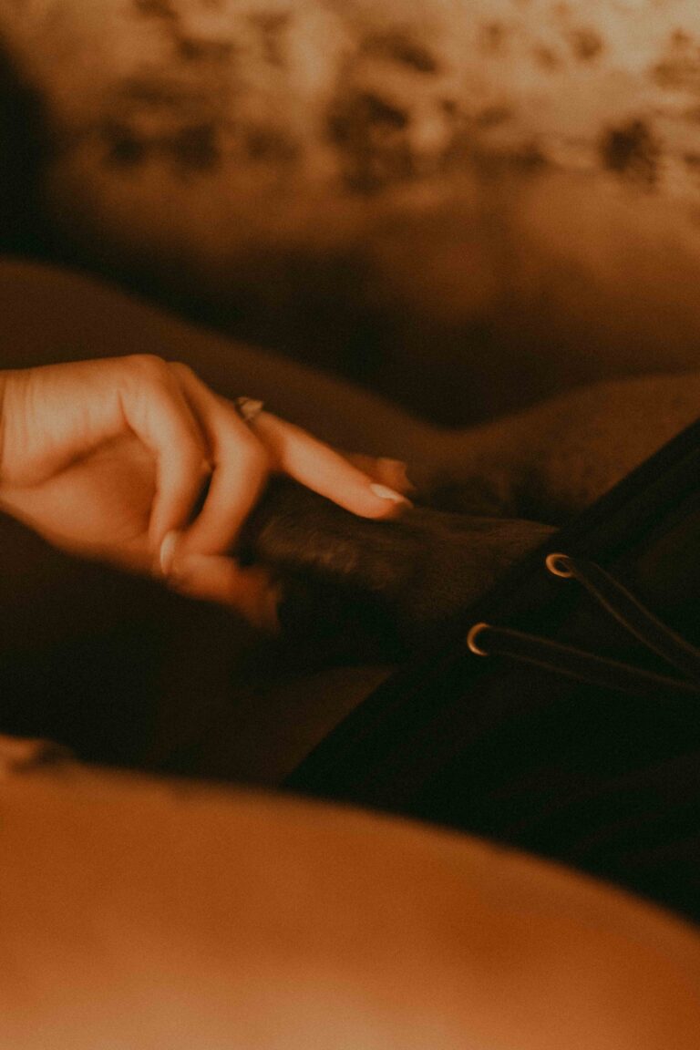 A hand caresses a furry object in a soft, warm environment with a blurred background, featuring a nude torso