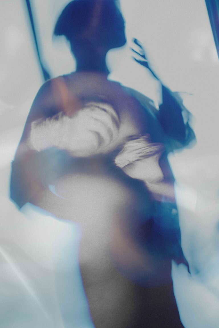 Blurred shadow of a naked person with a hand raised in artistic blue tones