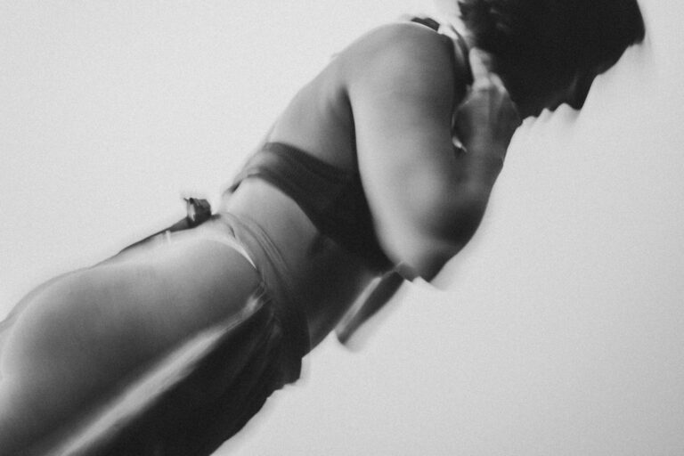 Een zwart-wit foto van een vrouw in een sportoutfit, die zich naar voren leunt met een dynamische en vloeiende houding.