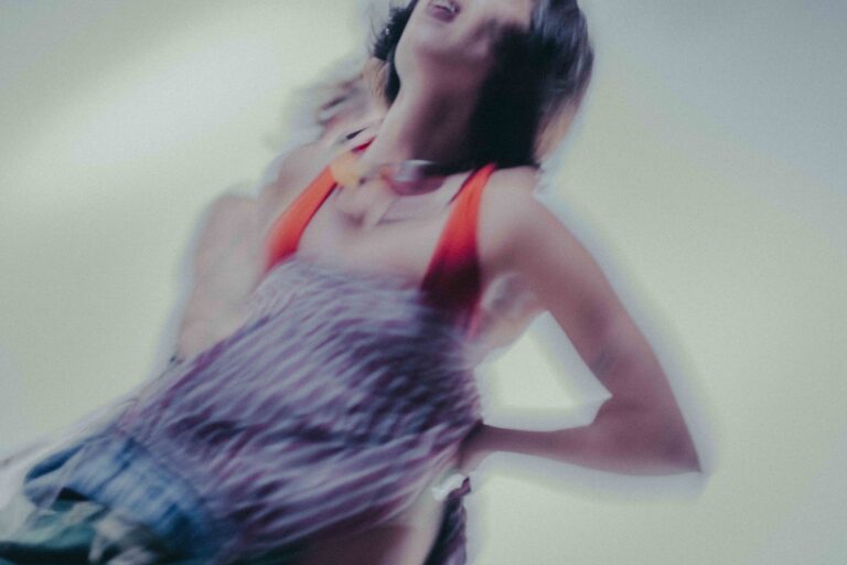 Een persoon in beweging met een rode top en een gestreepte blouse, tegen een wazige achtergrond, wat een gevoel van dynamiek en energie oproept.