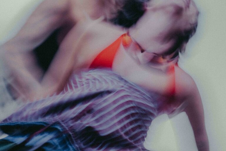 Een artistieke, bewogen afbeelding van een persoon in een rood topje, met een geabstraheerde achtergrond en een strakke, blauw-gestreepte jurk. De beweging creëert een dromerig effect.