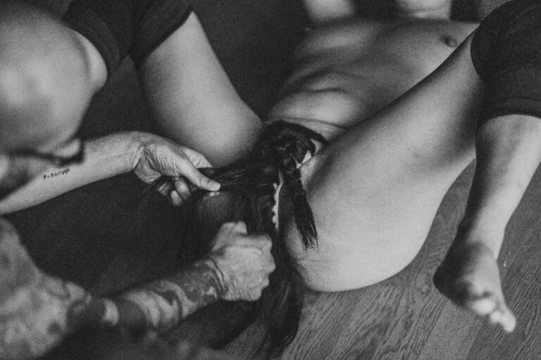 Een zwart-wit afbeelding van een vrouw met halflang haar die een man met een kaal hoofd en een baard aanraakt, terwijl hij zijn ogen gesloten heeft en een neutrale uitdrukking op zijn gezicht vertoont. De vrouw is deels uit beeld en draagt een zwart kledingstuk, terwijl de man geen bovenkleding draagt. De setting lijkt intiem en dicht bij de camera te zijn genomen.